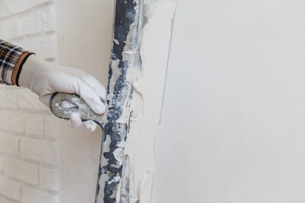 Worker in white gloves performs plastering of the walls of the room